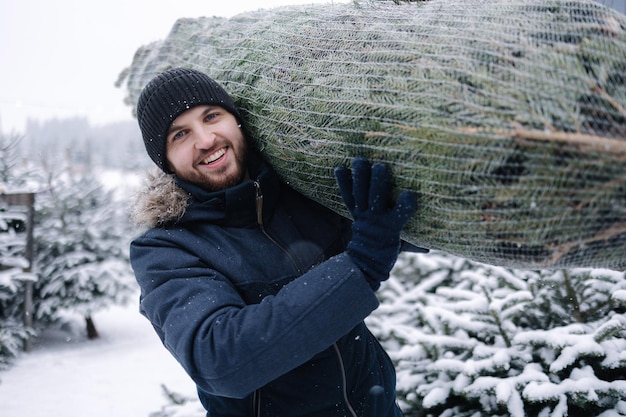 Retrato de hombre feliz lleva árbol de navidad del mercado de la tienda verde de árboles ecológicos embalaje de abeto