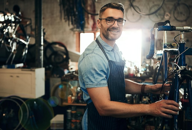 Retrato de hombre feliz o mecánico con bicicleta en un pequeño negocio para reparación, reparación o mantenimiento Técnico de bicicleta o ingeniero de bicicleta que trabaja en engranajes o hardware de vehículos de ciclismo en el taller