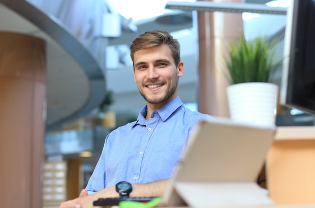 Retrato de hombre feliz sentado en el escritorio de oficina, mirando a cámara, sonriendo.