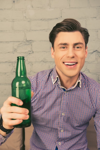 Retrato de hombre feliz sentado en el sofá con una botella de cerveza