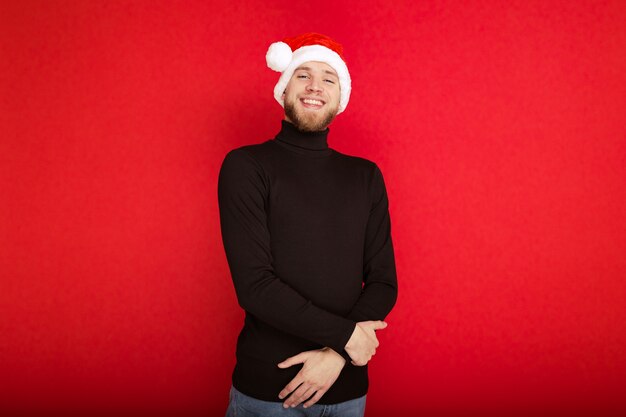 Retrato de un hombre feliz con un sombrero de Santa Claus sobre un fondo rojo.