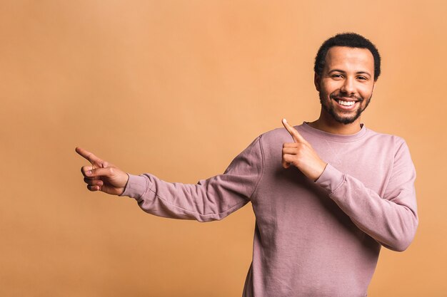 Retrato de un hombre feliz sonriente en casual apuntando con los dedos a un lado aislado sobre beige.