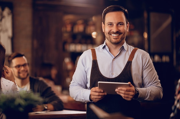 Retrato de un hombre feliz sosteniendo un panel táctil mientras trabaja a tiempo parcial como camarero en un pub