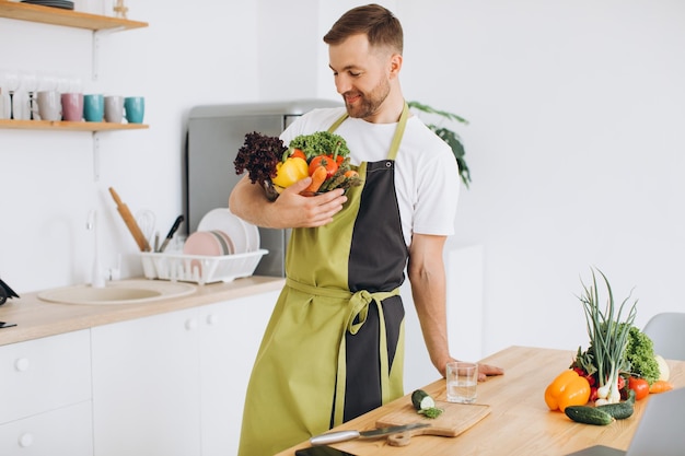 Retrato de un hombre feliz sosteniendo un plato de verduras frescas en la cocina