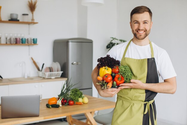 Retrato de un hombre feliz sosteniendo un plato de verduras frescas en el fondo de la cocina en casa