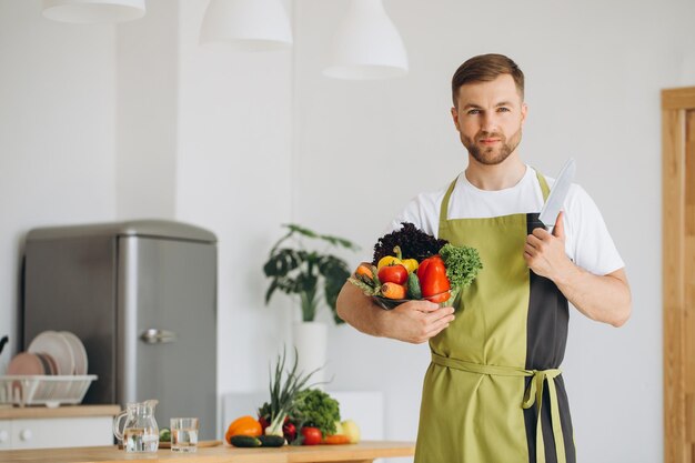 Retrato de un hombre feliz sosteniendo un plato de verduras frescas en el fondo de la cocina en casa