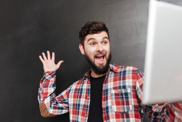 Retrato de hombre feliz vestido con camisa en una jaula saludando a sus amigos en Internet mientras usa una tableta