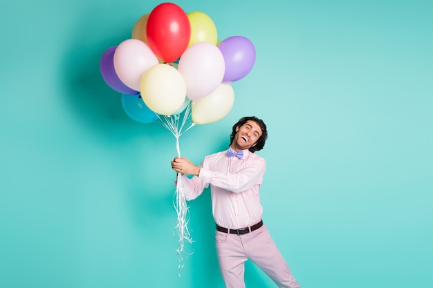 Retrato de hombre funky vestido con ropa formal mantenga globos de colores aislados sobre fondo de color turquesa