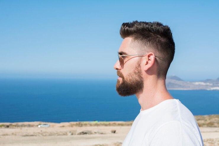 Retrato de un hombre con gafas de sol, barba y camisa blanca.