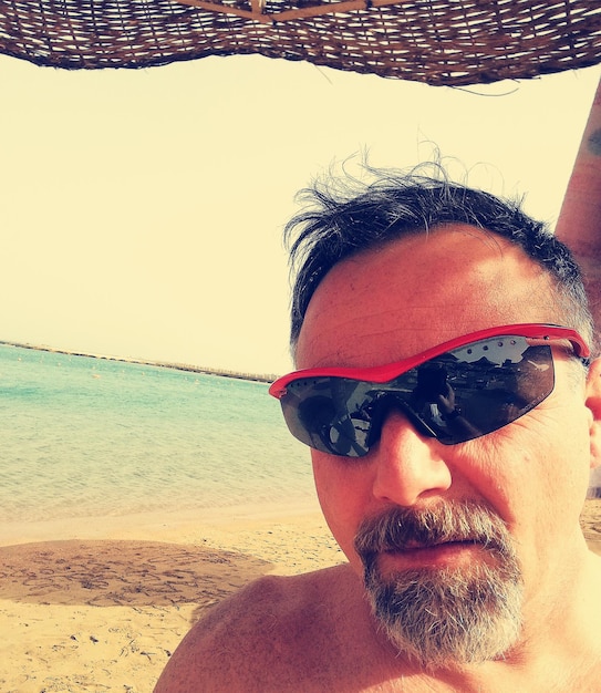 Foto retrato de un hombre con gafas de sol contra la playa