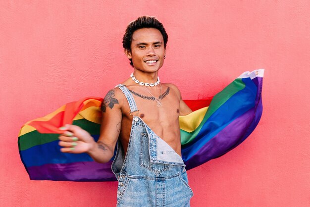 Foto retrato de un hombre gay sonriente sosteniendo una bandera contra la pared