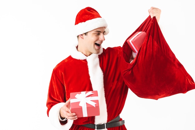 Retrato de hombre generoso de 30 años en traje de santa claus y sombrero rojo con bolsa festiva con cajas de regalo