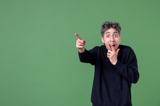 Retrato de hombre genio en tiro de estudio apuntando a distancia conmocionado en la pared verde