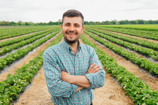 Retrato de un hombre de granjero barbudo moderno con los brazos cruzados mirando a la cámara se encuentra en el campo agrícola alegre trabajador masculino en agricultura agrícola agricultura agricultura