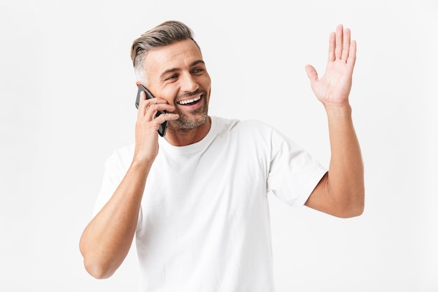 Retrato de hombre guapo de 30 años con camiseta casual con smartphone y conversación móvil aislado en blanco