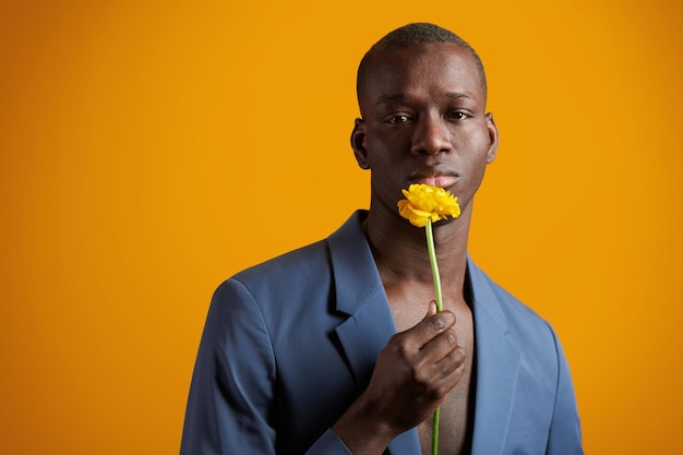 Retrato de hombre guapo africano en traje posando en cámara con flor aislado sobre fondo amarillo