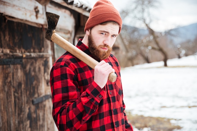 Retrato de hombre guapo con barba con hacha en la aldea