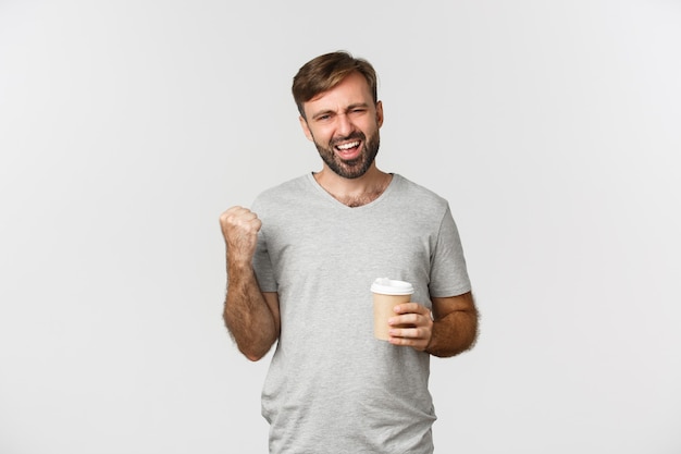 Retrato de hombre guapo con barba, vistiendo camiseta básica gris, sintiéndose con energía después de beber