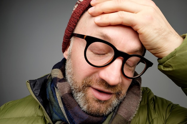 Retrato de un hombre guapo cansado y molesto con la cara inclinada de cerdas en la mano y mirando indiferente hacia abajo