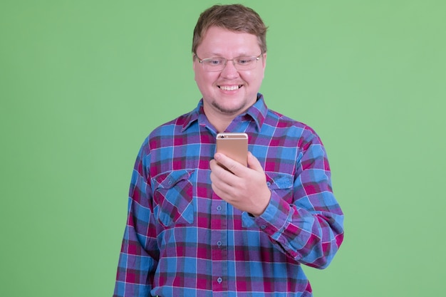 Retrato de hombre guapo hipster barbudo con sobrepeso con anteojos contra chroma key o pared verde