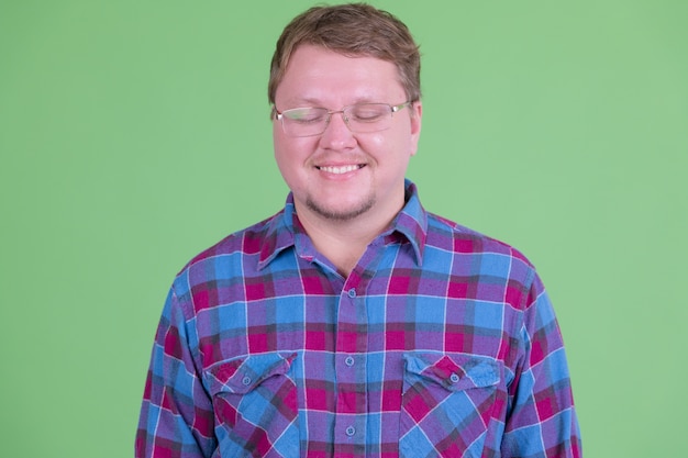 Retrato de hombre guapo hipster barbudo con sobrepeso con anteojos contra chroma key o pared verde