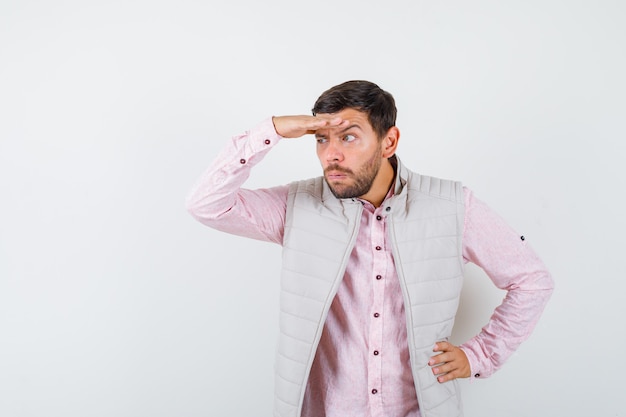 Retrato de hombre guapo mirando lejos con las manos sobre la cabeza en chaleco, camisa y mirando curioso