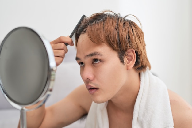 Retrato de hombre guapo mirándose en el espejo y cepillándose el pelo.