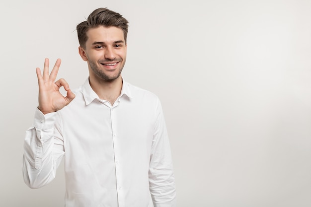 Foto retrato de hombre guapo mostrando signo ok contra el fondo blanco.