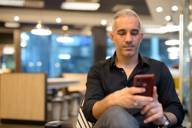 Retrato de hombre guapo sentado en la cafetería mediante teléfono móvil