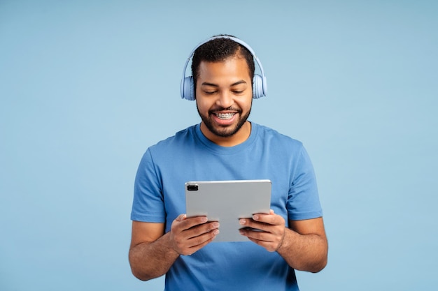 Retrato de un hombre guapo sonriente con auriculares sosteniendo una tableta digital escuchando música