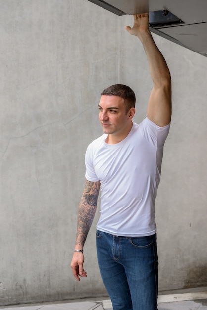 Retrato de hombre guapo con tatuajes contra la pared de hormigón