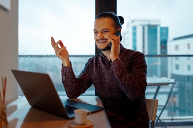 Foto retrato de un hombre guapo trabajando en una computadora portátil en el fondo de una ventana panorámica