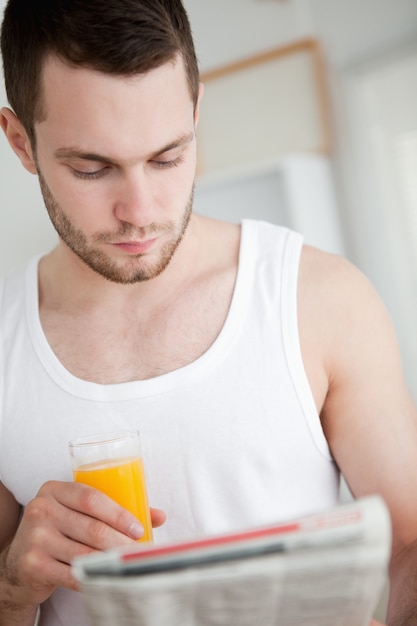 Retrato de un hombre hermoso bebiendo jugo de naranja mientras lee las noticias