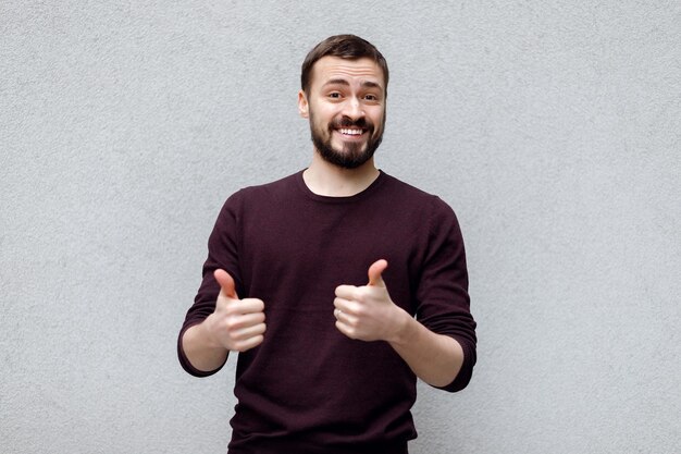 Retrato de hombre hipster emocional que muestra el dedo de clase en camiseta gris sobre fondo blanco.