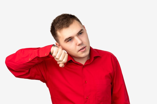 Retrato de hombre impaciente. Estrés de ansiedad. Chico preocupado en camisa roja escuchando reloj de pulsera aislado en blanco.