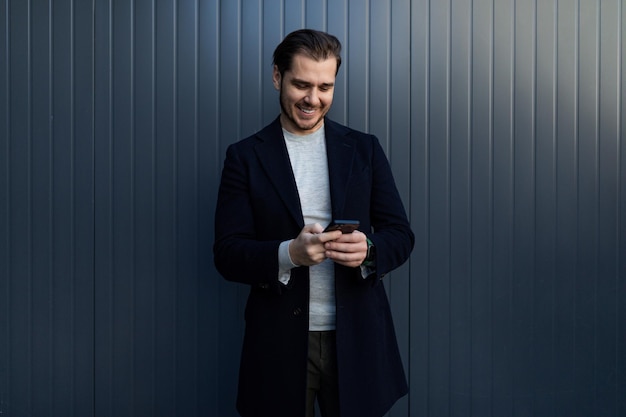 Retrato de un hombre independiente europeo sonriente con un teléfono inteligente en el contexto de un edificio