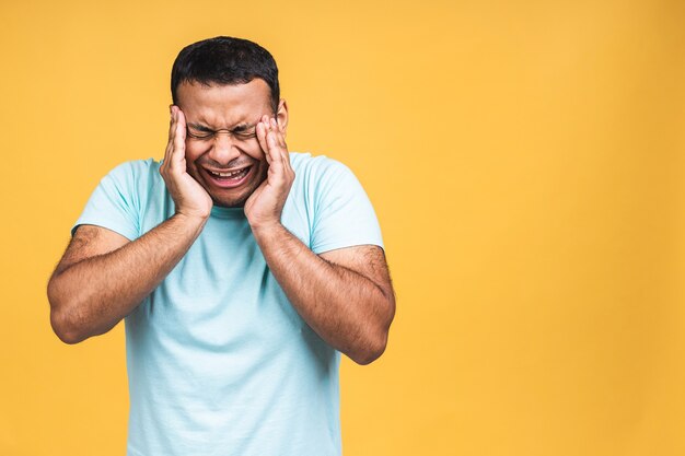 Retrato de hombre indio afroamericano infeliz y deprimido con cabello negro, manteniendo los ojos cerrados. Concepto de emociones y expresiones de rostro humano. Aislado sobre fondo amarillo.