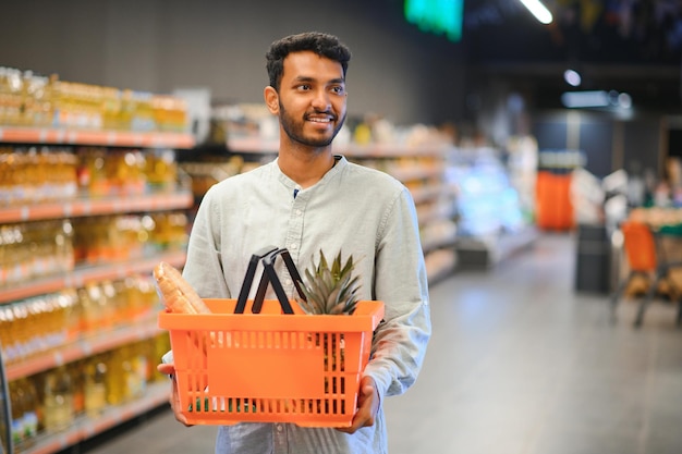 Retrato de un hombre indio feliz de pie frente al mostrador de productos en una tienda de comestibles Un hombre comprando comestibles para casa en un supermercado