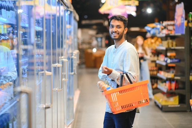 Retrato de un hombre indio feliz de pie frente al mostrador de productos en una tienda de comestibles Un hombre comprando comestibles para casa en un supermercado