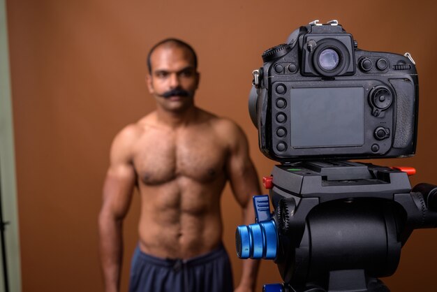 Retrato de hombre indio musculoso con bigote vlogging sin camisa con cámara