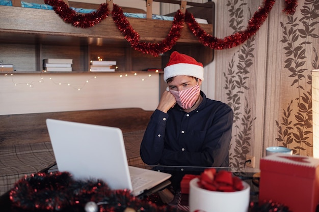 Retrato de hombre infeliz con máscara sentado en la habitación cerca de decoraciones navideñas