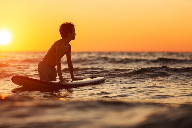 Retrato de hombre joven en el agua con tabla de windsurf al atardecer