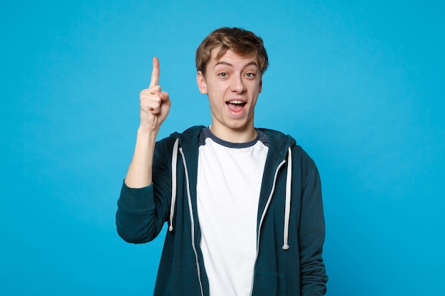 Retrato de hombre joven alegre emocionado en ropa casual mantenga el dedo índice hacia arriba con una gran idea nueva aislada en la pared azul. Personas sinceras emociones, concepto de estilo de vida.