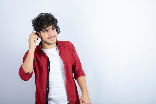 Retrato de hombre joven en auriculares escuchando canciones sobre pared blanca.