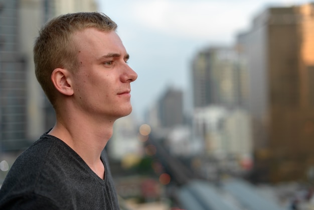 Retrato de hombre joven con cabello rubio contra la vista de la ciudad al aire libre