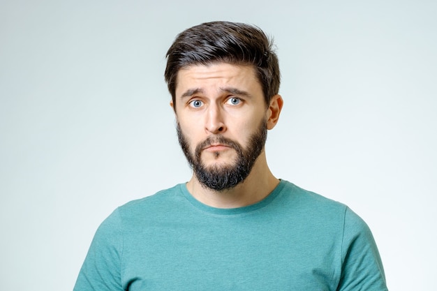 Retrato de hombre joven con expresión de la cara triste aislado sobre fondo gris