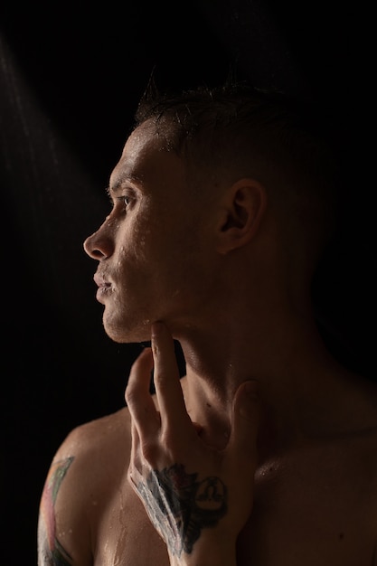 Retrato de hombre joven con gotas de agua en la cara sobre fondo oscuro