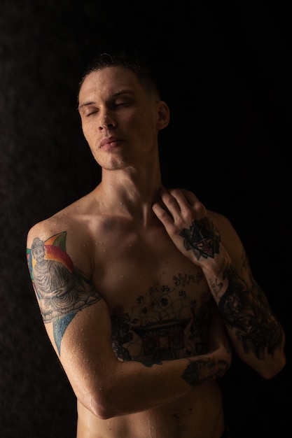 Retrato de hombre joven con gotas de agua en la cara sobre fondo oscuro