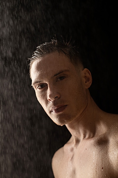 Foto retrato de hombre joven con gotas de agua en la pared negra