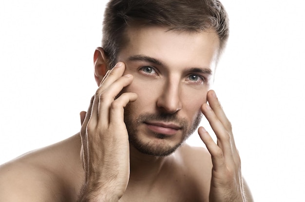 Retrato de hombre joven y guapo con piel suave posando sobre fondo blanco.